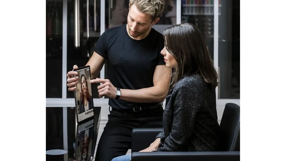 A woman sits in a hair salon chair consulting her stylist on what hair colour suits
