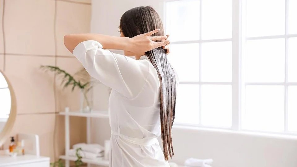 Woman applies a L’Oréal Professionnel hair serum from the roots to the ends of the hair]