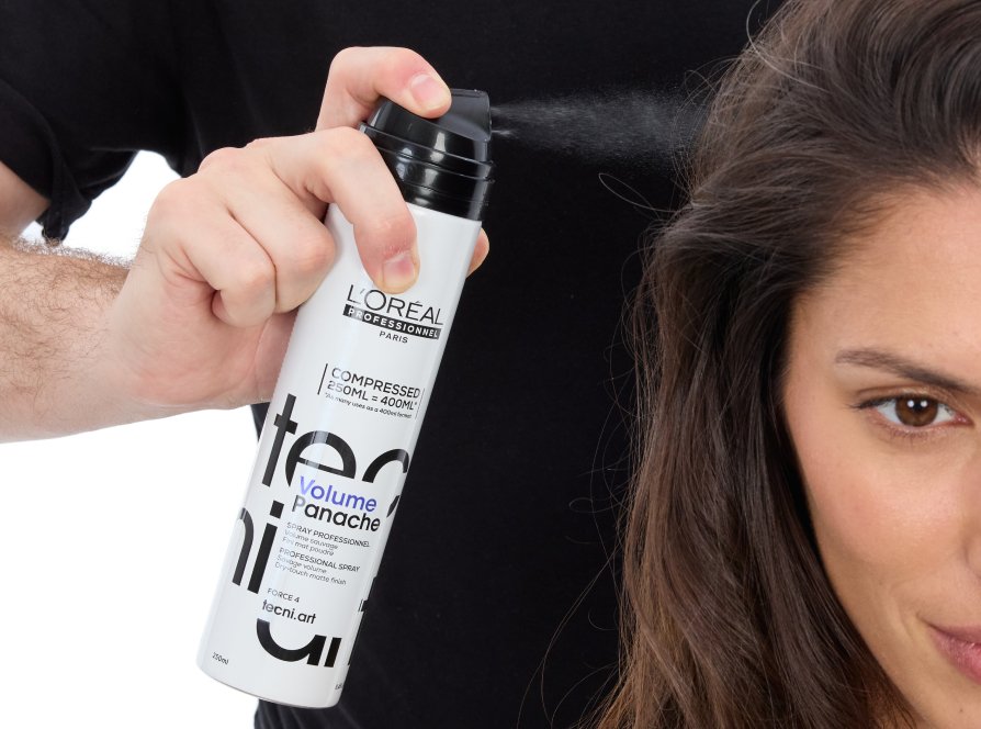 Focus on a woman’s long hair gaining volume as a professional stylist uses volumizing spray, following the latest hairstyle trend